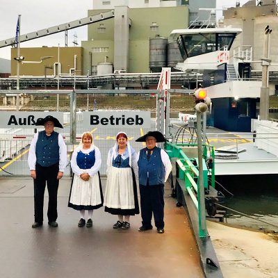 Mitglieder der Altriper Trachtengruppe begrüßen die neue Rheinfähre.